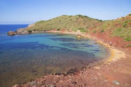 Der Sand am Playa de Cavalleria hat eine rötliche Färbung.